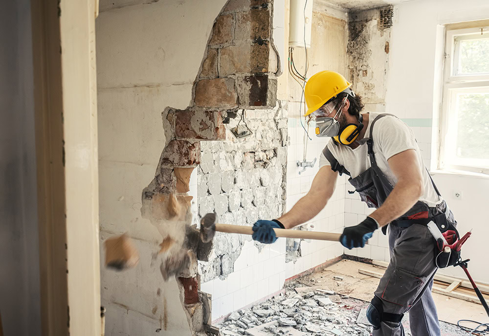 A man uses a sledge hammer to break down a partitioning wall.